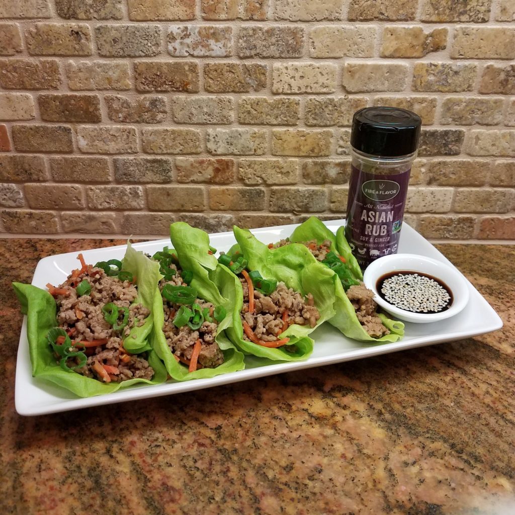 3 lettuce wraps with meat and spices in them and a side of soy sauce with seeds in it