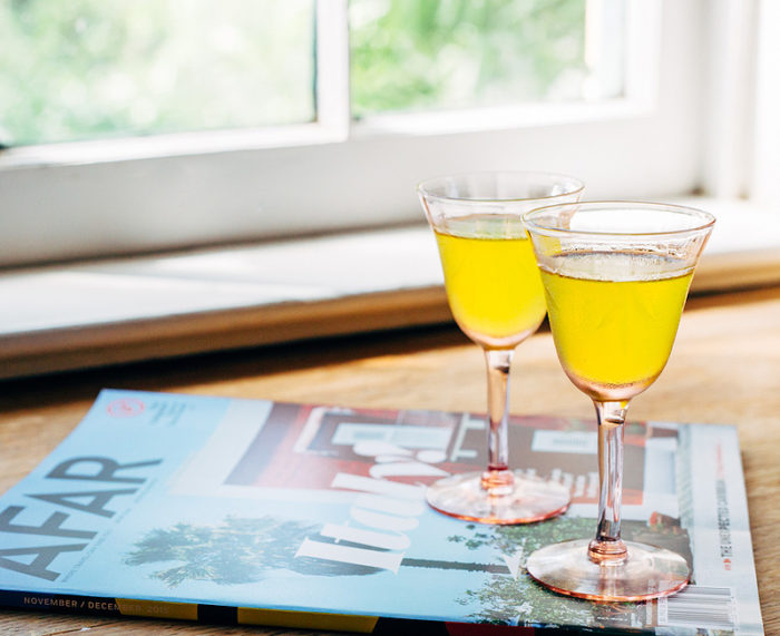 Two glasses of limoncello on top of a travel magazine about Italy